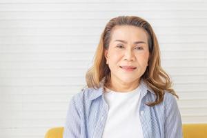 retrato de mulher asiática feliz na sala de estar, relaxante mulher madura de meia idade olhando para a câmera foto