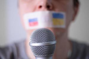 uma boca com fita adesiva com uma bandeira da rússia e da ucrânia tentando falar em um microfone. foto