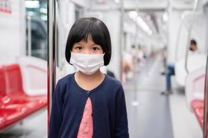 menina com máscara cirúrgica proteção facial contra gripe e surto de vírus em transporte público skytrain ou metrô. conceito de novo estilo de vida normal, usando o transporte público para viajar para a escola. foto