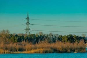 rede elétrica alcançando a floresta pelo lago azul foto