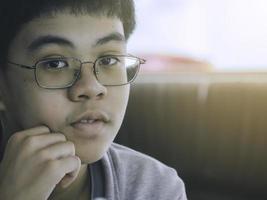 menino pensativo usando óculos com roupa casual pensando com um balão de pensamento vazio. foto