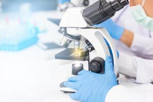 as mãos de homens usando luvas de borracha azuis estão usando um microscópio para trabalhar no laboratório.