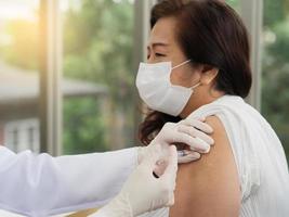 close-up de uma médica usando luvas e usando uma seringa com algodão para vacinar uma paciente de meia-idade, vacina covid-19 ou coronavírus. foto