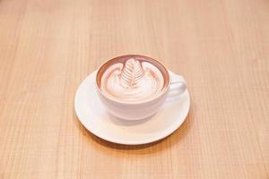 café quente com leite de folha fofa em copo branco na mesa de madeira, leia para servir. foto