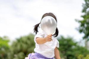 menina segurando o balão branco na frente do rosto no jardim. foto