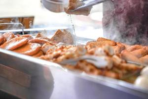 O palito de bola de carne de peixe chikuwa está fervendo na panela grande, na loja de comida local do japão para venda. foto