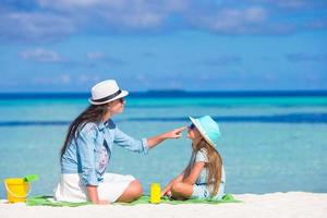 mãe aplicando creme de proteção solar para sua filha na praia tropical foto