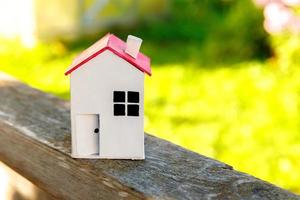 casa modelo de brinquedo branco em miniatura em fundo de madeira perto de pano de fundo verde. aldeia ecológica, abstrato ambiental. conceito de ecologia em casa de sonho de seguro de propriedade de hipoteca imobiliária. foto