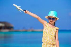 menina feliz com avião de brinquedo nas mãos na praia de areia branca foto