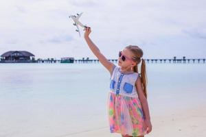 menina feliz com avião de brinquedo nas mãos na praia de areia branca