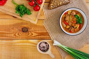 ensopado com carne e legumes em molho de tomate em fundo de madeira. vista do topo foto