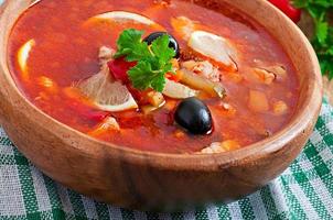 sopa solyanka russo com carne, azeitonas e pepinos em tigela de madeira foto