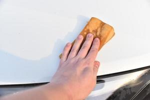 lavando um carro branco com uma esponja à mão foto