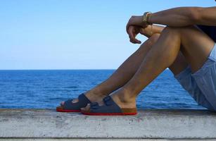 as pernas do homem com cena de praia de sandálias nas férias de verão foto