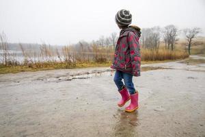 menina com botas cor de rosa andando em um caminho lamacento foto