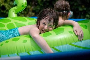 sorridente jovem feliz descansando no flutuador de piscina vibrante na piscina ensolarada do quintal foto