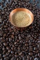 xícara de cobre cheia de café expresso no centro de grãos de café crus espalhados na mesa rústica foto