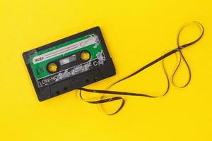 antiga fita cassete retrô com etiqueta grunge cercada por pilha de fita puxada em fundo amarelo foto