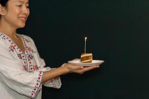 mão de uma mulher segurando um pedaço de bolo de aniversário no prato com vela. foto