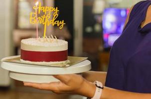 mulher segurando o bolo de aniversário com vela e prato de aniversário.