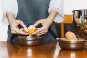 padeiro feminino com avental quebrando um ovo prepare-se para assar na mesa de madeira foto