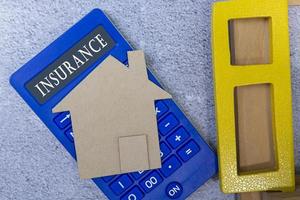texto de seguro na calculadora com modelo de casa de papel e moldura de janela em uma mesa foto