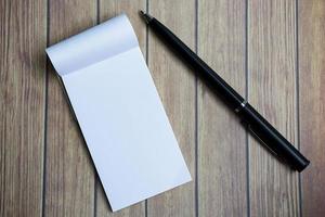 bloco de notas com uma caneta em uma mesa de madeira. diretamente acima. postura plana. foto