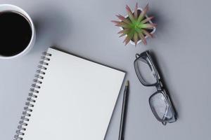 bloco de notas com xícara de café, óculos, caneta e vaso de plantas em uma mesa. postura plana