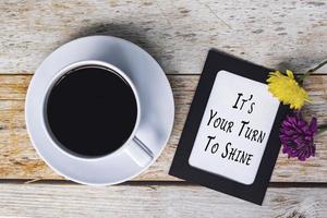 citação motivacional na moldura de quadro-negro e xícara de café branco na mesa de madeira. foto