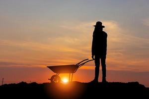 silhueta de trabalhador com carrinho de mão ao pôr do sol, homem agricultor com carrinho de mão vazio com traçado de recorte foto