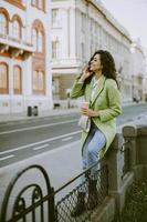 jovem mulher usando smartphone na rua e segurando café para viagem foto