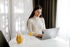 jovem mulher usando um laptop e bebendo suco de laranja saudável