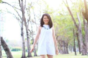 linda mulher asiática de vestido branco relaxa e sorrindo no parque natural. menina tailandesa ou menina chinesa desfrutar de férias no jardim foto