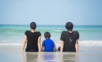 família asiática sentada na praia olhando para o mar azul, a ilha, a luz do sol e o céu azul da manhã. foto