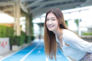 jovem mulher bonita asiática cabelos longos sorrisos brilhantes e fica na esteira ao ar livre da cidade foto