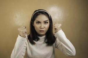 linda garota asiática está brava e zangada com punho de braços isolado em fundo laranja. foto