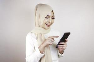 retrato de alegre jovem muçulmana asiática sorrindo enquanto olha para seu celular foto