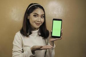 felizes e sorridentes jovens mulheres asiáticas mostrando uma tela verde em branco. foto