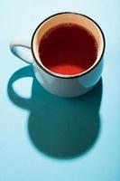 uma xícara de chá preto sobre fundo azul sob a luz do sol.