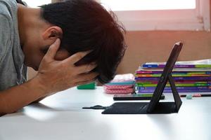 homens asiáticos com dores de cabeça do trabalho em casa, homem se sentindo cansado, entediado e com sono sentado na mesa. ele olhando para o computador pensando em trabalho na sala de estar em casa, home office devido à pandemia covid19 foto