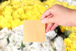 papel de nota em branco na mão sobre fundo de buquê de flores de crisântemos lindos brancos e amarelos, cópia-espaço no cartão para colocar sua mensagem. foto