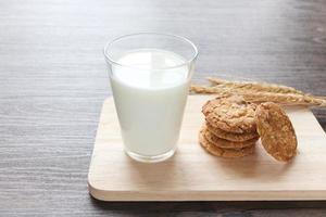 deliciosos biscoitos de aveia com espigas e copo de leite na tábua de madeira na mesa. foto