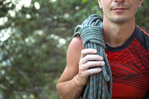 um alpinista masculino de aparência caucasiana com uma corda enrolada no ombro. mão em magnésia branca. camisa esportiva vermelha, esportes radicais, escalada. espaço para texto foto