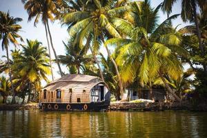 navio de cruzeiro de prazer casa-barco na índia, kerala, nos canais do rio cobertos de algas de allapuzha, na índia. barco no lago sob o sol brilhante e palmeiras entre os trópicos. vista casa-barco foto