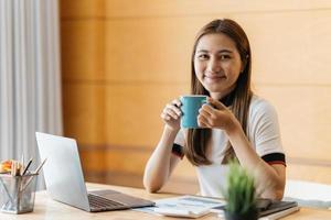 jovem relaxando e bebendo uma xícara de café ou chá quente usando o computador portátil em um dia frio de inverno no quarto mulher verificando aplicativos sociais e trabalhando conceito de comunicação e tecnologia foto