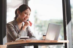 jovem segurando o cartão de crédito e usando o computador portátil. empresária trabalhando em casa. compras online, e-commerce, internet banking, gastar dinheiro, trabalhar em casa conceito foto