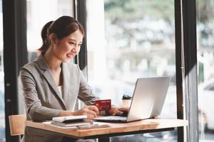 jovem segurando o cartão de crédito e usando o computador portátil. empresária trabalhando em casa. compras online, e-commerce, internet banking, gastar dinheiro, trabalhar em casa conceito foto