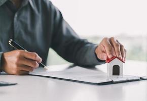 feche a casa de brinquedo de madeira com o homem assina um contrato de compra ou hipoteca para uma casa, conceito imobiliário. foto