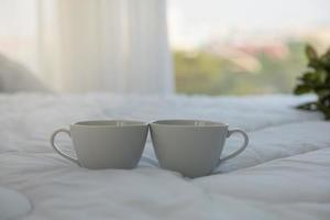 close-up de duas xícaras de café branco quente na cama no quarto com espaço de cópia pela manhã. foto