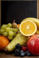 frutas frash, laranja, maçã, banana, pêra, uvas contra o quadro-negro foto
